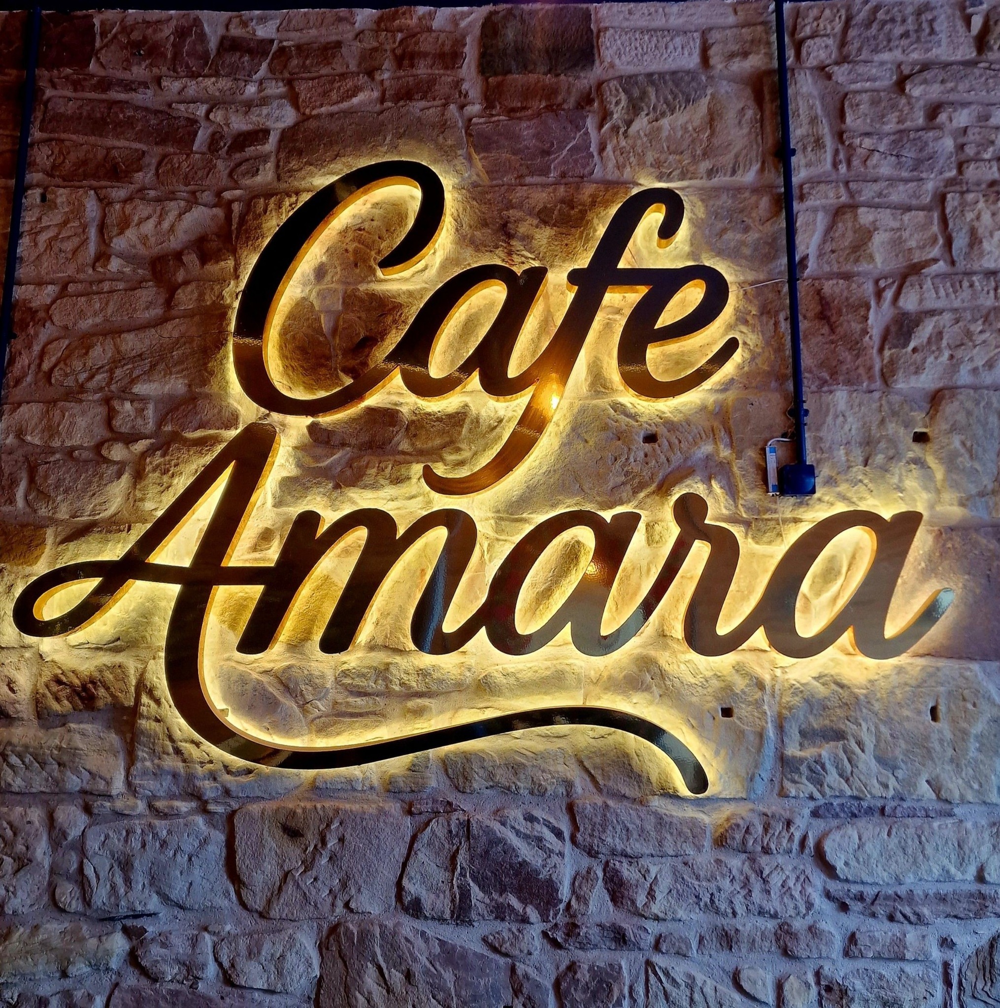 Cafe Amara illuminated gold sign on exposed stone wall inside the cafe