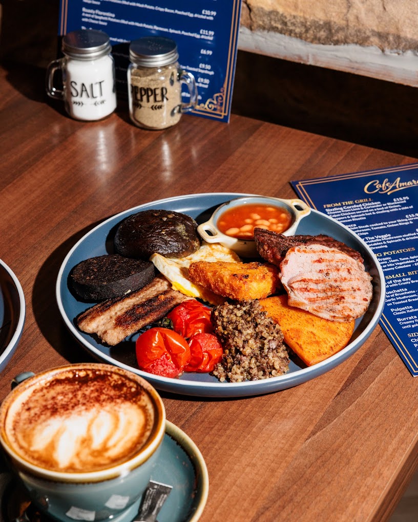 A hearty full Scottish breakfast with coffee served on a wooden table at Cafe Amara