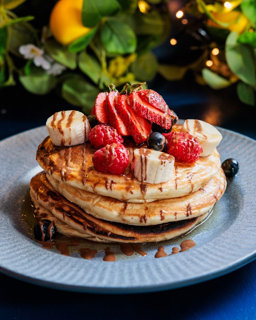 Fluffy American pancakes topped with fresh strawberries, banana and maple syrup