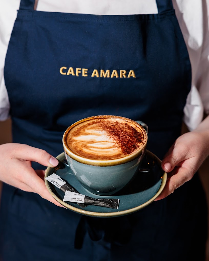 Barista holding a beautifully crafted cappuccino wearing a Cafe Amara apron
